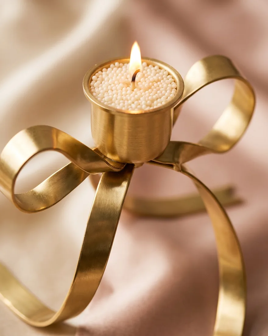 Close-up of the Gold Bow Stand: the candle cup, ivory sand-wax pearls and the flame above the bow knot