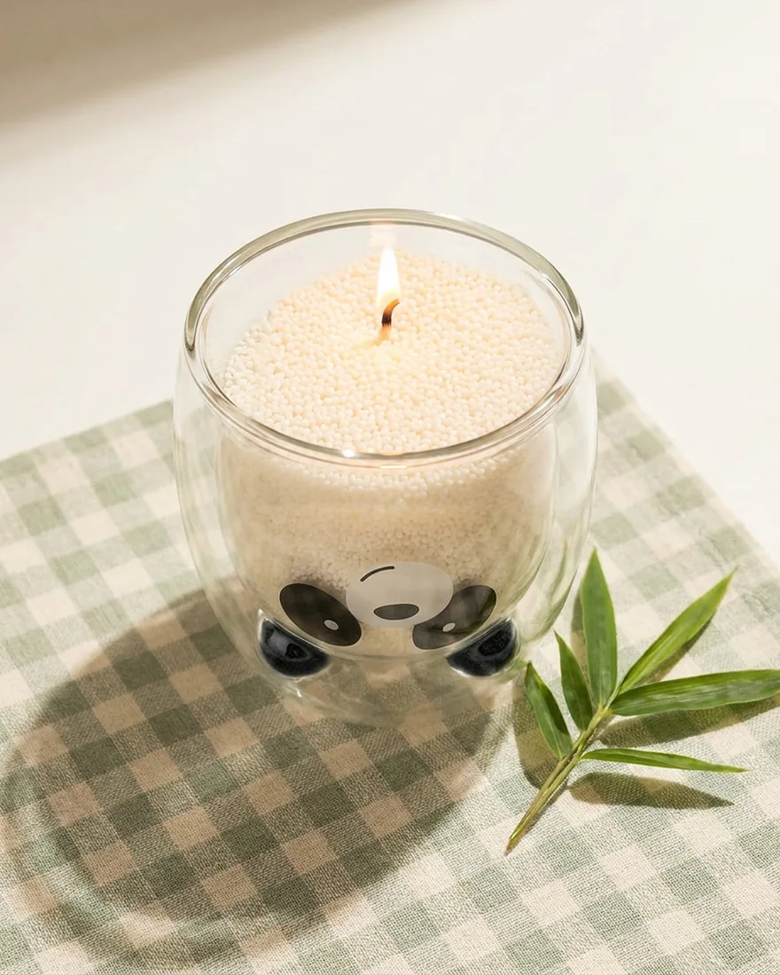 The Panda Glass Candle seen from above on gingham cloth, the sand wax and flame inside the glass
