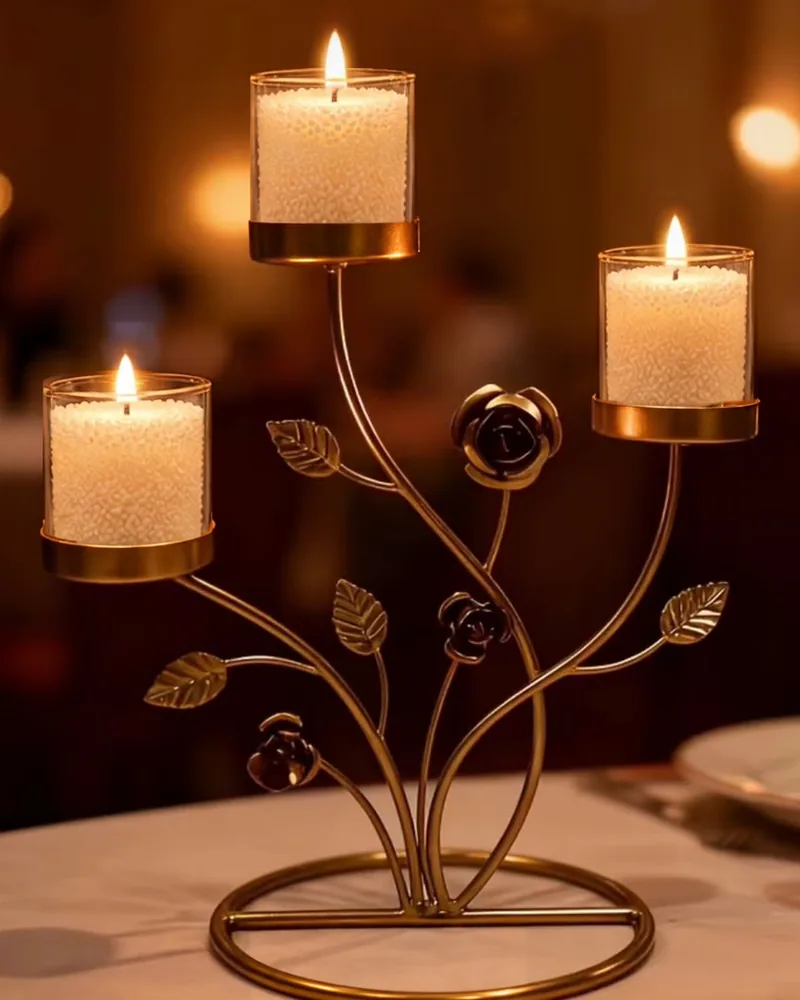 Three jars of ivory sand wax, lit, in a gold rose-branch candle stand